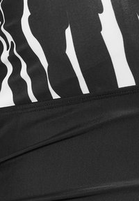 Svart baddräkt med vita vågiga ränder, med en texturerad kvalitet och en figursydd design. Inkluderar en stilren svart midjeband i botten.