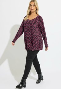 Maglietta a maniche lunghe, dalla vestibilità ampia, di colore viola scuro con motivo floreale rosa e dettagli con bottoni, abbinata a pantaloni neri aderenti e stivali neri lucidi.