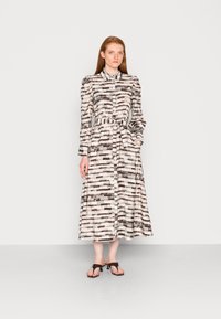 Vestido longo com um fecho de botões na frente, feito de um tecido leve e com um padrão riscado em preto, branco e bege, de forma abstrata e suave.