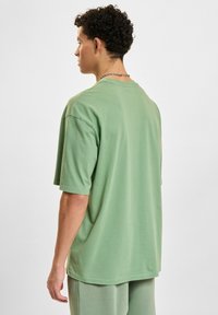 Korte mouwen, oversized T-shirt van zachtgroene katoen. Ronde halslijn, ontspannen silhouet en een gladde textuur met minimale details.