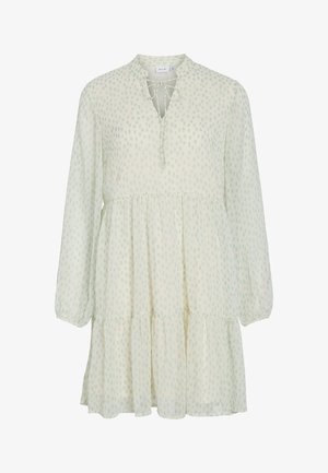 Rochie crem deschis cu mâneci lungi, cu buline verzi subtile, fustă stratificată, decolteu în V și închidere cu fundă în față la gât.