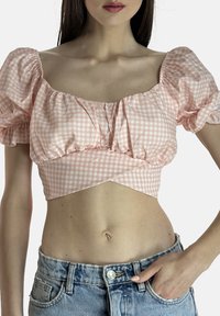 Pink ternet crop top med puffærmer og indsnævret talje. Kombineret med slidte lyseblå denimjeans, der fremhæver en tætsiddende silhuet.