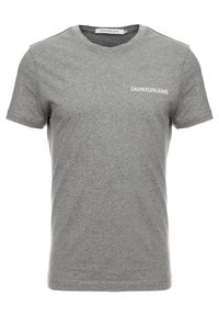 Šedé bavlněné tričko s krátkými rukávy, kulatým výstřihem a bílým logem "CALVIN KLEIN JEANS" na levé straně. Hladká textura po celé ploše.