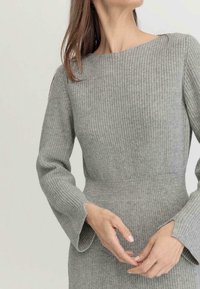 Abito grigio a coste con scollo a barca e maniche lunghe a campana, con vita aderente e tessuto dalla texture interessante. Mani posizionate con dolcezza.