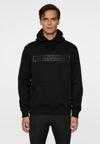 Musta huppari, jossa on nyörityksellä varustettu huppu, kengurupocket ja mattamusta logo edessä. Ribbaatut hihansuut ja helma viimeistelevät suunnittelun.