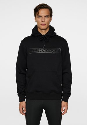 Le hoodie noir présente une capuche à cordon de serrage, une poche kangourou et un logo noir mat sur le devant. Des poignets et un ourlet côtelés complètent le design.