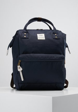 Granatowy plecak Anello z podwójnymi górnymi uchwytami, przednią kieszenią na zamek, bocznymi taśmami zamka błyskawicznego oraz brązowymi regulowanymi paskami na ramię.