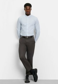 Hellblaues Hemd mit Kragen und Knopfleiste, kombiniert mit dunkelbraunen Hosen und schwarzen Schuhen, ausgestattet mit einer glatten Textur und maßgeschneiderter Passform.