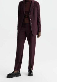 Vínově červený oblek na míru s jednorušovou bundou se třemi knoflíky, zúženými kalhotami a černými mokasínami s tlustou podrážkou.