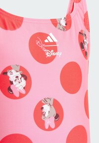 Roze zwemkleding met grote rode stippen en cartoonfiguren. Bevalt Adidas- en Disney-logo's in het wit. Gladde, rekbare stof.