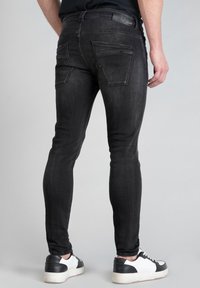 Jean en denim noir avec une coupe slim, comportant deux poches arrière et des détails de couture subtils. Associés à des baskets blanches.