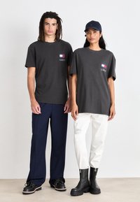 Camisetas de algodón gris con un pequeño logo, combinadas con pantalones azul marino y blanco. Botas negras con suela gruesa en un modelo. Colores sólidos.