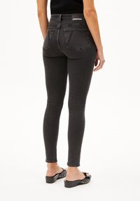 Jean skinny noir avec taille haute et design à cinq poches. Doté d'une texture lisse et d'un patch logo au dos. Porté avec des sandales à talons noires.