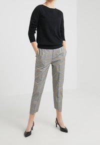 Pull noir à manches longues associé à un pantalon à carreaux gris avec des accents jaunes, coupe droite et longueur raccourcie. Chaussures à talons noires.