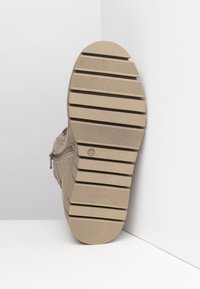 Bottine beige avec une tige en suede texturé, équipée d'une fermeture éclair sur le côté et d'une semelle en caoutchouc durable avec des rainures horizontales pour l'adhérence.