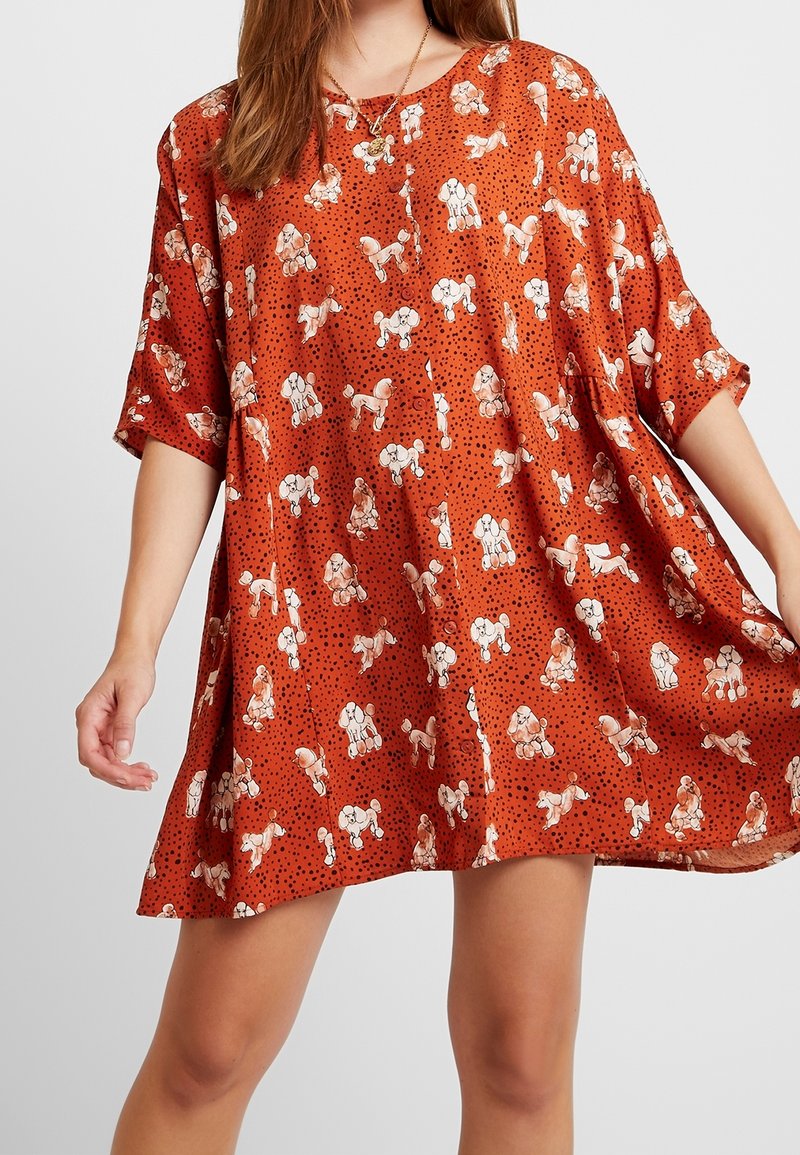 Robe à manches courtes et coupe ample en tissu orange avec des motifs ludiques de chiens et des pois noirs. Comprend un col rond et un ourlet fluide.