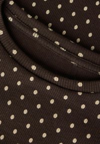 Brunt ribbestrikket stoff med lyse beige polkadotter. Teksturen er strikket, med rund hals og brettet kantdetalj.