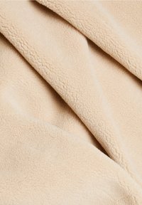 Beige fleece-tyg med en mjuk, strukturerad yta, som har en slät finish och subtila fiberlinjer genom materialet.