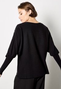 Czarny sweter dziergany o luźnym kroju, z rękawami balonowymi i ściągaczami. Tył jest prosty, bez widocznych wzorów czy akcentów.