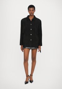 Giacca camicia in suede nero con dettagli a frange, chiusura con bottoni argentati e due tasche frontali. Texture liscia e vestibilità sagomata.
