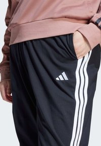 Črne športne hlače z belo trojno črtasto dekoracijo, izdelane iz lahkega blaga. Imajo elastičen pas in stranske žepe.