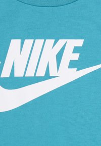 Tyrkysové bavlněné tričko s velkým bílým logem "NIKE" a designem vlny. Hladká textura s kulatým výstřihem.