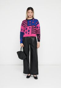 Strikket genser med rosa, blå og svarte farger med stjerne- og stripe mønstre; kombinert med vide svarte fake skinnbukser og en svart veske.