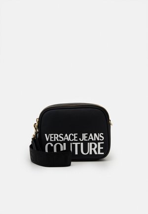 Zwarte rechthoekige crossbodytas met gouden ritssluiting en "Versace Jeans Couture" in grote witte letters gedrukt aan de voorkant.