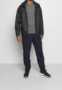 Černá lehká bunda s kapucí, šedé tričko a námořnické kalhoty. Sportovní boty s černobílými detaily dokončují outfit.