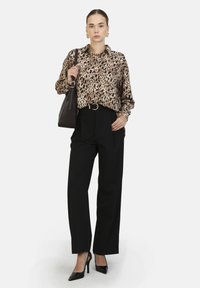 Camicia a righe di leopardo, pantaloni neri a vita alta, décolleté nere, collana a catena e borsa nera con tracolla.
