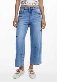 Jeans a gamba larga in denim azzurro chiaro con ricami di Topolino e piccoli dettagli neri, vita alta e stile a cinque tasche.