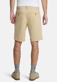 Shorts beige a mezza lunghezza realizzati in tessuto leggero, dotati di due tasche posteriori con bottoni e design frontale piatto.