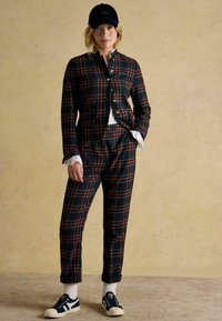 Pledēts kostīma komplekts tumši zilā, zaļā un sarkanā tonī; pieguļošs žakete ar zelta pogām, atbilstošas bikses; kopā ar tumši zilām kurpēm un baltām zeķēm.