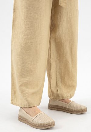 Chaussures beiges tissées à enfiler avec semelles plateformes texturées portées avec un pantalon ample en lin beige clair, vue de mi-mollet jusqu'aux pieds.