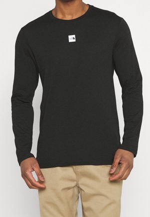 Camiseta negra de manga larga de algodón suave con cuello redondo, con un logotipo blanco cuadrado en el pecho y mangas ajustadas.