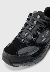 Close-up of gray and black athletic shoe with thick sole, textured fabric, and lace-up fastening.