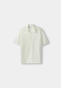 Kurzarmhemd mit Kragen in Cremeweiß, das aus einem strukturierten, waffelartigen Stoff besteht und über eine Knopfleiste sowie einen geraden Schnitt verfügt.