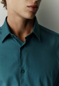 Turquoise button-up shirt with a subtle vertical striped pattern, made from smooth fabric; features pointed collar and black buttons.