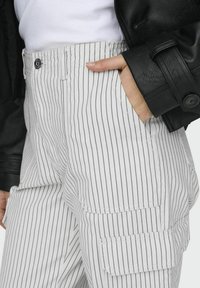 Witte gestreepte cargobroek met een relaxte fit, voorzien van zijzakken en een vlakke tailleband, gecombineerd met een zwarte leren jas.