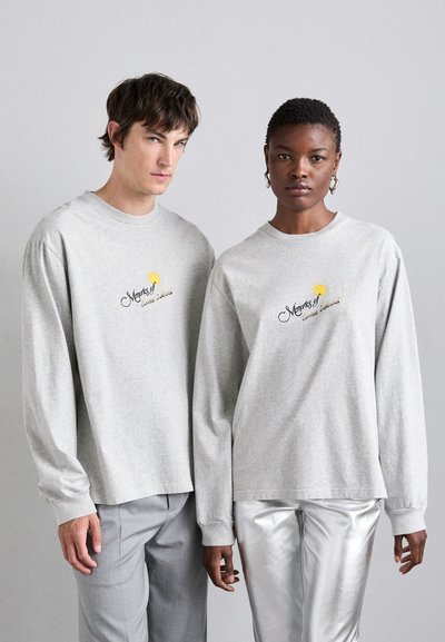 Gray long sleeve shirts featuring a logo design on the front. The fabric appears soft, with relaxed fits on both individuals.