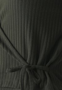 Tissu côtelé vert foncé avec une surface texturée, doté d'un détail de nœud à la taille. Semble doux et ajusté.