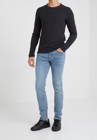 Long-sleeve dark gray shirt, light blue fitted jeans, and black sneakers. Casual attire with a simple design, no visible patterns or accents.