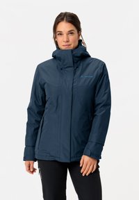 Navy wasserdichte Jacke mit hohem Kragen, verstellbarer Kapuze und seitlichen Reißverschluss-Taschen. Merkmale sind eine glatte Textur und ein Logo-Akzent.