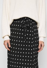 Jupe noire à pois avec une ceinture à nouer. Tissu léger, longueur genou, dotée de pois blancs régulièrement espacés et d'une texture lisse.