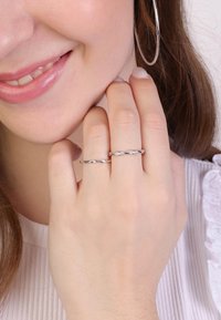 Silver rings on two fingers; one has a twisted design, while the other features smooth, engraved accents; model's hand rests on her face.
