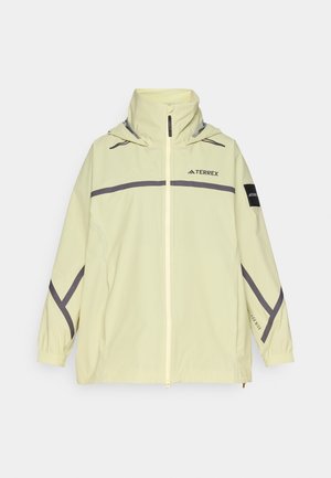 Hele kollane veekindel jope esitsepiga, reguleeritava kapuutsiga, hallide aktsentidega ja elastsete mansettidega. Ees on logo rinnal ja varrukal.