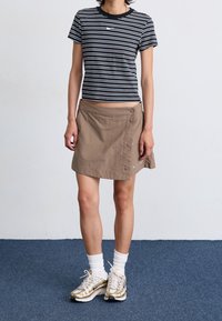 Pasiasta czarno-biała koszulka z krótkim rękawem, khaki spódnica kopertowa z guzikami, białe skarpetki sportowe i sneakersy ze złotymi akcentami.