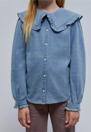 Jasnoniebieska koszula denimowa z dużym falbaniastym kołnierzem, zapięciem na guziki z przodu oraz delikatnym haftem kwiatowym. Długie rękawy z falbaniastymi mankietami.