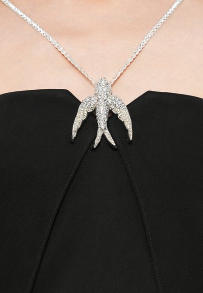Sølvfuglevedhæng med krystalpynt på en delikat kæde, båret over en sort, tekstureret strapless top.