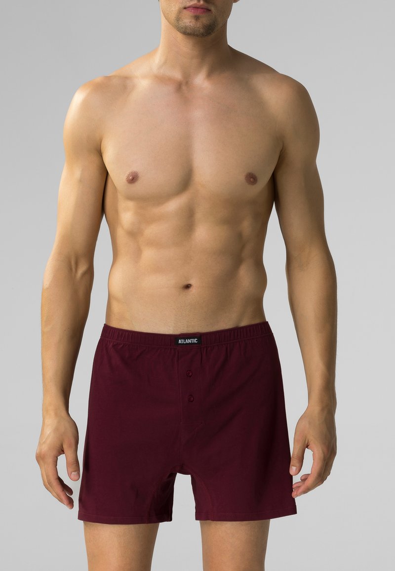 Burgundowe bokserki wykonane z miękkiego materiału, z elastycznym pasem i dwoma guzikami z przodu. Gładka faktura i klasyczny krój.